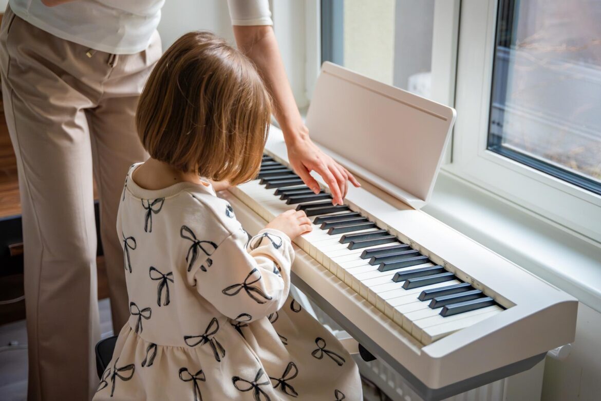What is music theory? The Moving Parts Behind a Song An adult points to keys on a white digital piano while a seated girl watches.