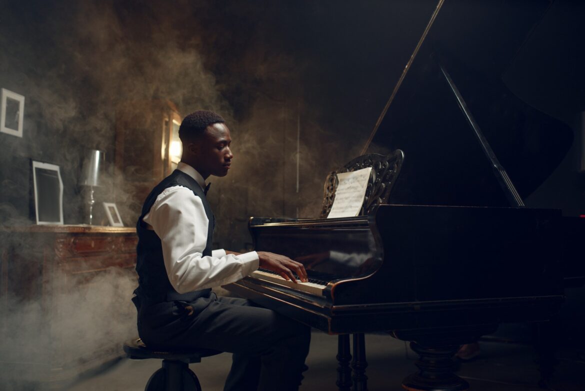 A pianist in a white shirt and dark vest plays a black grand piano with both hands.