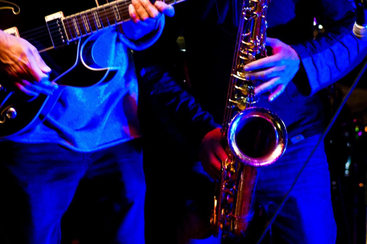 Amplified Jazz Fusion: Where Groove Meets Improvisation Close-up of musicians playing electric guitar and saxophone under blue stage lighting.