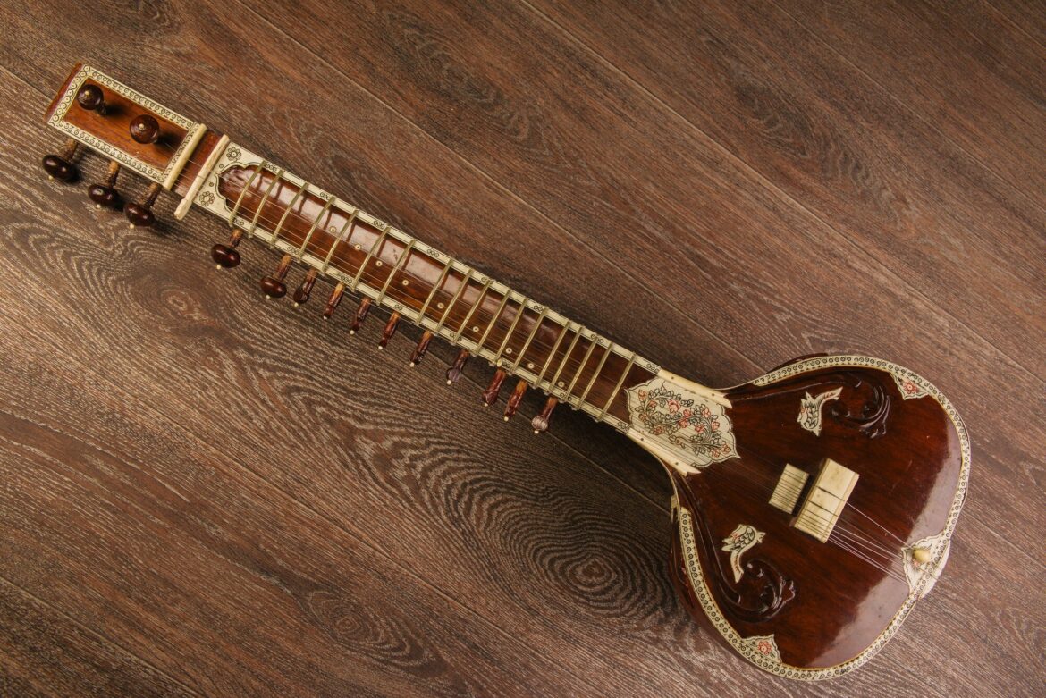 An ornately decorated sitar lies diagonally on a wooden floor.