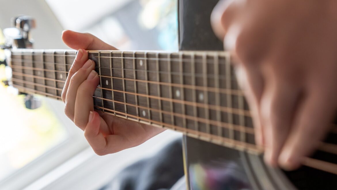 Pentatonic Scale: From Five Notes to Musical Phrases Close-up of hands playing an acoustic guitar, with the fretboard beside a bright window.