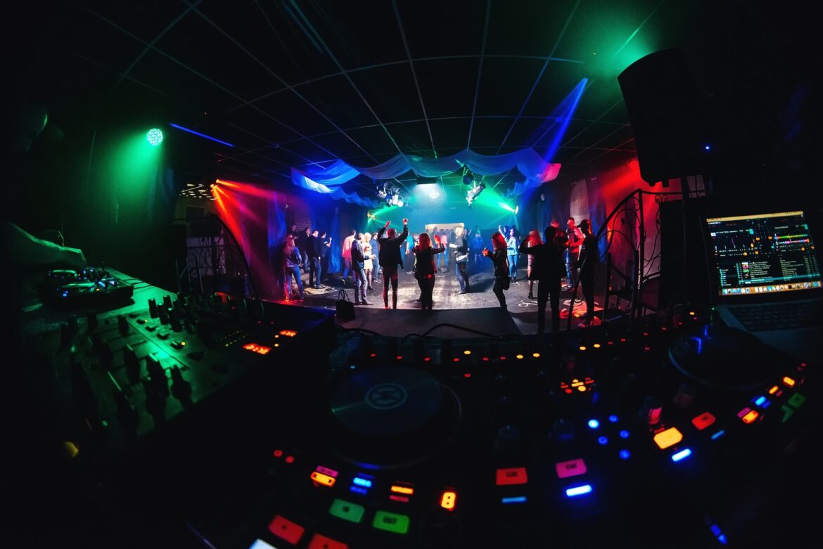 House Music: Chicago Roots, Steady Pulse, Shifting Groove DJ equipment overlooking people dancing in a dark nightclub under colorful lights.