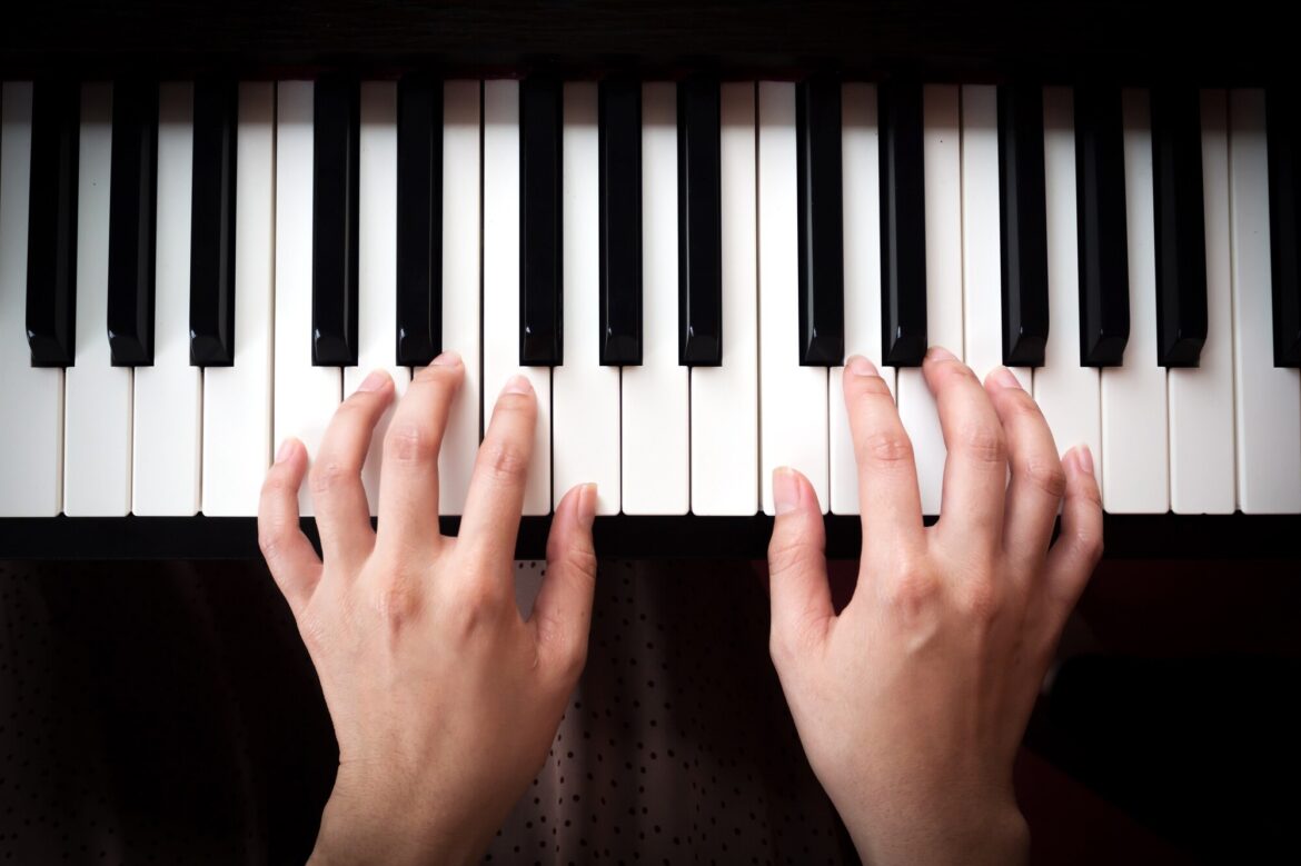 Overhead view of two hands playing an unmarked piano keyboard.