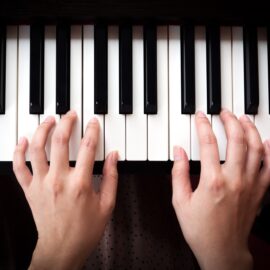 Overhead view of two hands playing an unmarked piano keyboard.