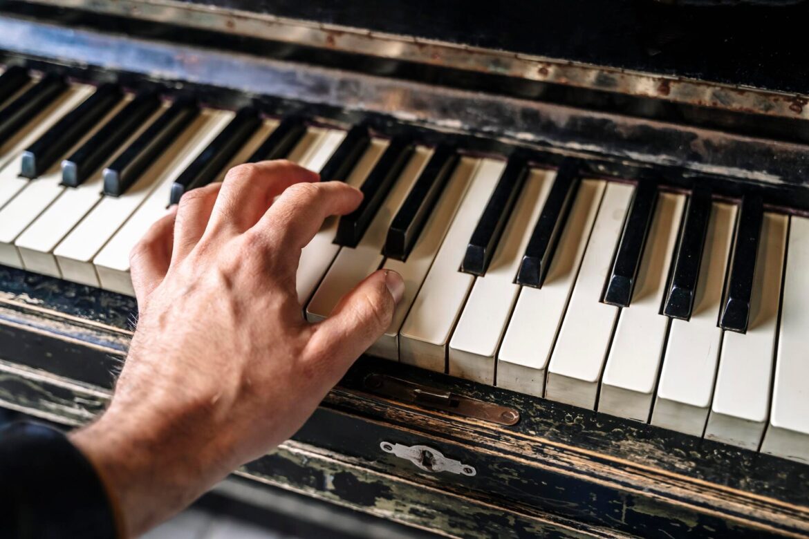 A hand spans separated keys on a worn black-and-white piano keyboard.