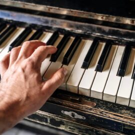 A hand spans separated keys on a worn black-and-white piano keyboard.