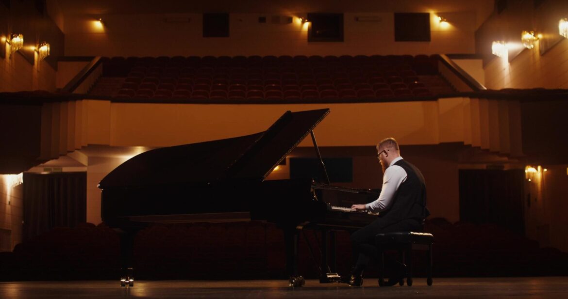 Classical Music Composers: 12 Accessible First Works A pianist plays a black grand piano onstage in a warmly lit concert hall.